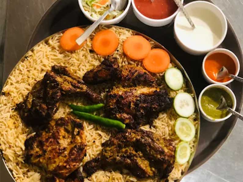 A serving of mandhi rice topped with tender grilled meat, presented alongside traditional condiments, set within the inviting interior of Beirut Mandhi in Iritty, Kerala. Beirut Mandhi Iritty